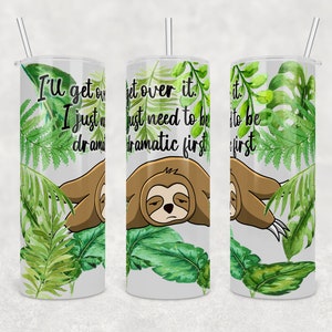 Puede incluir: Un vaso blanco con un diseño de hojas tropicales verdes y un gráfico de perezoso. El vaso tiene el texto "I'll get over it. I just need to be dramatic first." impreso en él.