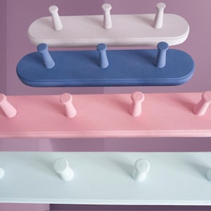 May include: Four wooden wall-mounted coat racks in different pastel colours: light blue, pink, blue, and white. Each rack has five hooks.