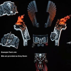 May include: A collection of grey resin miniature components featuring a sword, shoulder pads with lion and shield motifs, winged attachments, and braziers with orange flames. The set includes detailed skull emblems and gothic architectural elements.