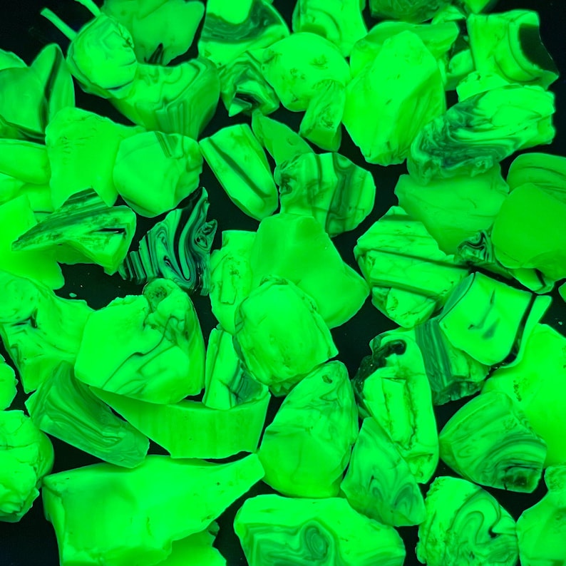May include: A collection of irregularly shaped, glowing green stones. The stones have a marbled appearance with dark green and black swirls. The background is a dark, solid color, creating a contrast with the bright stones.
