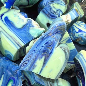 May include: A collection of irregularly shaped, polished stones with a marbled appearance. The stones feature swirling patterns of blue, white, and pale green, creating a dynamic and textured surface. The overall effect is reminiscent of ocean waves or abstract art.