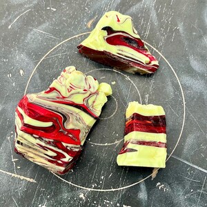 May include: Three abstract, colorful, rock-like sculptures. The pieces feature a mix of red, yellow, and brown hues, with a marbled effect. The shapes vary in size and form, creating a unique artistic display.