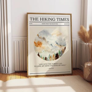 May include: A framed print titled "THE HIKING TIMES" with a watercolour illustration of a forest and mountains. The print includes the quote "AND INTO THE FOREST I GO TO LOSE MY MIND AND FIND MY SOUL" by John Muir. The frame is a light brown colour.