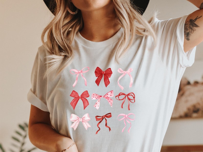 Op de afbeelding: Wit T-shirt met een afbeelding van roze en rode strikken. De strikken zijn in verschillende stijlen en maten.