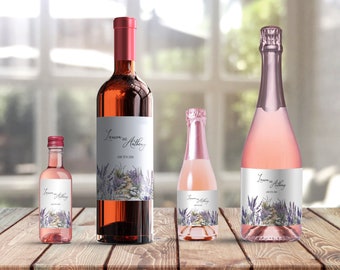 Può includere: Quattro bottiglie di vino con etichette personalizzate che presentano un design ad acquerello di fiori di lavanda e un sentiero di pietra. Le etichette includono i nomi "Lauren e Anthony" e la data "15 giugno 2024".
