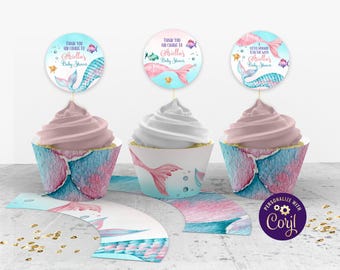 May include: Set of cupcake wrappers and toppers with a mermaid theme. The wrappers are pink and blue with a mermaid tail design. The toppers are round and feature a mermaid with the text "Thank you for coming to Ariellas Baby Shower".