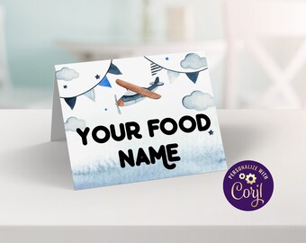 Puede incluir: Una tarjeta plegada con un diseño de acuarela que presenta un avión azul y marrón, nubes y banderines. El texto "YOUR FOOD NAME" se muestra en letras negras en negrita. Un círculo púrpura con el texto "PERSONALIZE WITH Corjl" está en la esquina inferior derecha.