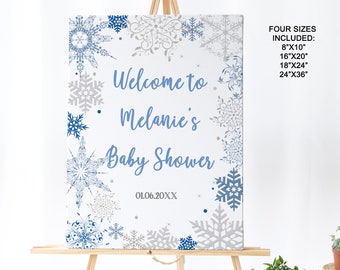 Puede incluir: Un letrero de baby shower con un diseño de copo de nieve. El letrero dice "Bienvenida a la fiesta de bienvenida de Melanie" en escritura azul. El letrero está decorado con copos de nieve azules y plateados sobre un fondo blanco.