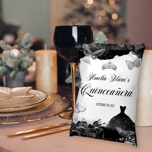 May include: A white cushion with black and silver accents features a butterfly design and the text "Amelia Marie's Quincea&ntilde;era September 24th, 2023".