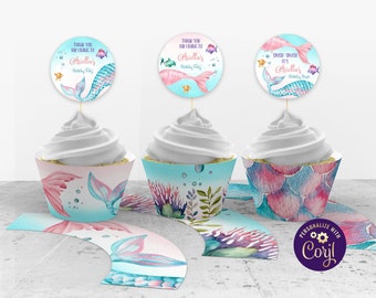 May include: Mermaid themed cupcake wrappers and toppers with a pink and blue watercolor design. The toppers feature a mermaid tail with the text "Thank you for coming to Ariellas Birthday Party" and "Splash Splash It's Ariellas Birthday Bash".