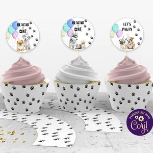 Puede incluir: Conjunto de envoltorios para cupcakes con un patrón de huellas de patas y tapas a juego con un tema de perros. Las tapas presentan ilustraciones de acuarela de perros y globos con el texto "Reagan is One" y "Let's Pawty".