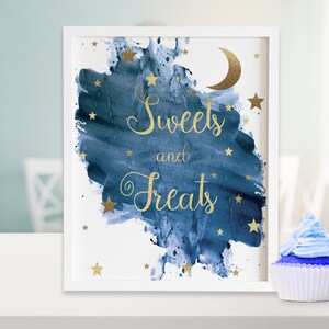 May include: A framed print with the words "Sweets and Treats" in gold script, set against a blue watercolor background with gold stars and a crescent moon. A cupcake with blue frosting sits nearby.