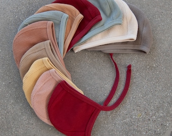 May include: A collection of baby bonnets in various colors, including red, yellow, and blue. The bonnets are made of a textured fabric and have ties under the chin. The bonnets are arranged in a circular pattern.