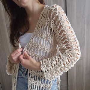 Könnte beinhalten: Ein gehäkeltes Cardigan in Cremefarbe mit einem zarten Lochmuster. Das Cardigan hat lange Ärmel und eine lockere Passform.