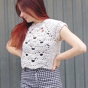 Puede incluir: Un top blanco de crochet con manga corta y un diseño festoneado. El top es corto y tiene un escote redondo.