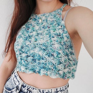 May include: A handmade, halter-neck crochet top in shades of blue, teal, and white. The top has a scalloped edge and a textured, openwork design. The garment is a summer top.