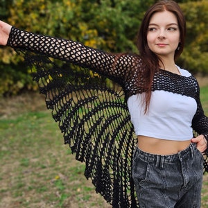 May include: A black crochet top with long sleeves and a wide, open neckline. The top is made of a delicate, lacy fabric and has a flowing, ethereal look.