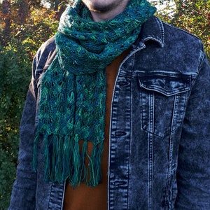 May include: A green and blue crocheted scarf with fringe. The scarf is worn around the neck of a person wearing a denim jacket.