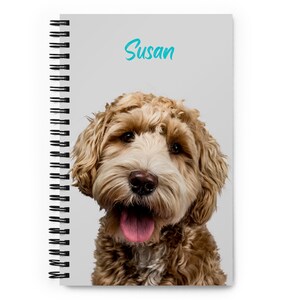 May include: A spiral bound notebook with a light grey cover featuring a close-up photo of a brown and white dog with its tongue sticking out. The dog's name, "Susan", is written in turquoise lettering at the top of the cover.