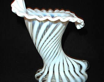 May include: A white and blue swirled glass vase with a ruffled rim. The vase has a flared base and a twisted, elongated body. The rim is scalloped and the vase is set against a black background.