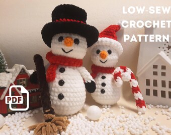 Puede incluir: Un patrón de crochet para hacer dos muñecos de nieve. El patrón se llama "Low-Sew Crochet Pattern" y está disponible para descargar en PDF. Los muñecos de nieve son blancos con ojos y botones negros, bufandas rojas y sombreros negros. Un muñeco de nieve sostiene un bastón de caramelo.