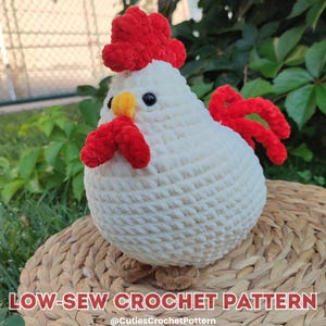 May include: A white crocheted chicken with a red comb and wattle. The chicken is sitting on a woven basket. The image includes the text "LOW-SEW CROCHET PATTERN @CutiiesCrochetPattern".