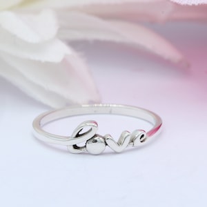 May include: A silver ring with the word "love" spelled out in a cursive font.