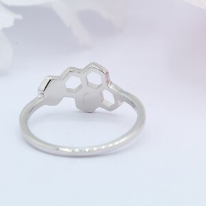 May include: A silver ring featuring a honeycomb design. The ring is simple and elegant.