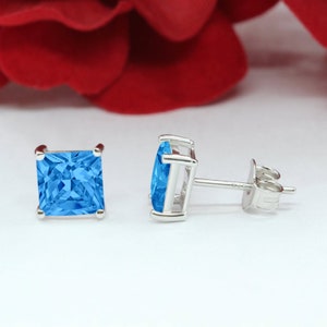 May include: A pair of silver stud earrings with a square shaped blue topaz gemstone.