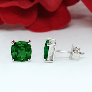 May include: A pair of silver stud earrings with emerald green square-shaped gemstones.