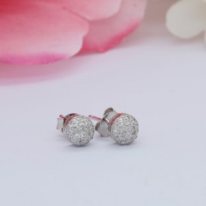 May include: A pair of silver stud earrings with a round, sparkly design. Each earring is set with small, clear stones.