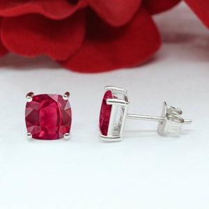 May include: A pair of silver stud earrings with a square red gemstone in each earring.