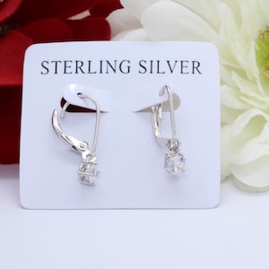May include: Sterling silver earrings with a clear cubic zirconia stone on each earring. The earrings are on a white card with the text "Sterling Silver" printed on it.