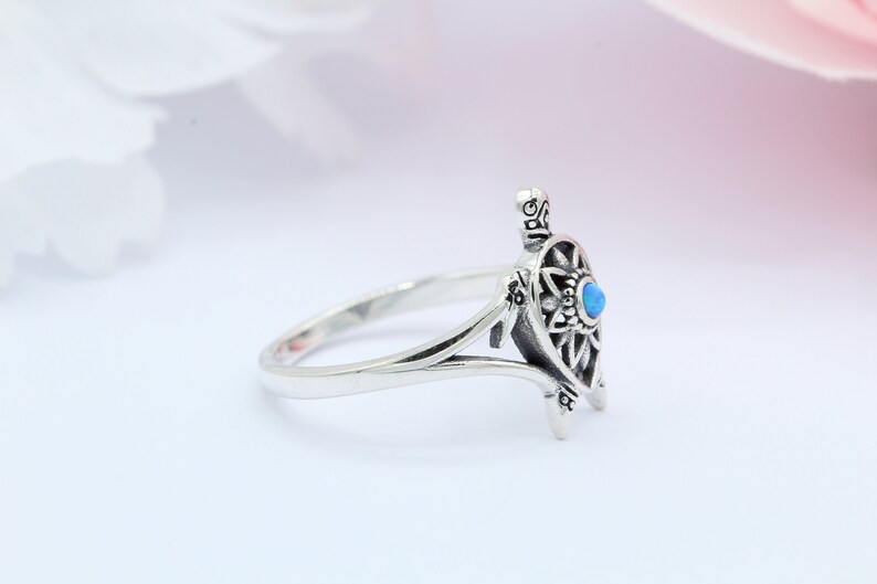 May include: A silver ring with a detailed turtle design and a blue opal gemstone. The ring is open and has a delicate band.