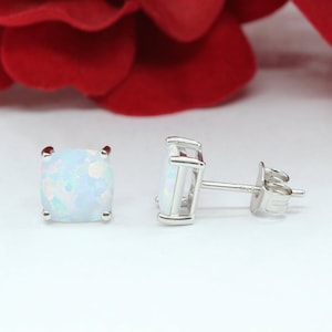 May include: A pair of silver stud earrings with white opal gemstones. The earrings have a square shape and are set in a simple, elegant design.