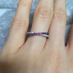 May include: A silver band ring with a double row of small stones. The top row is made of clear stones, and the bottom row is made of pink stones.