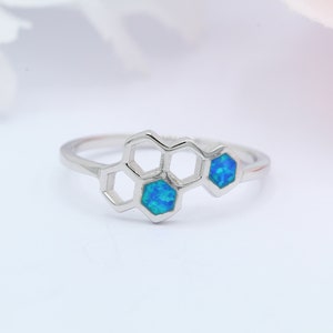 May include: A silver ring featuring a honeycomb design with two blue opal stones.