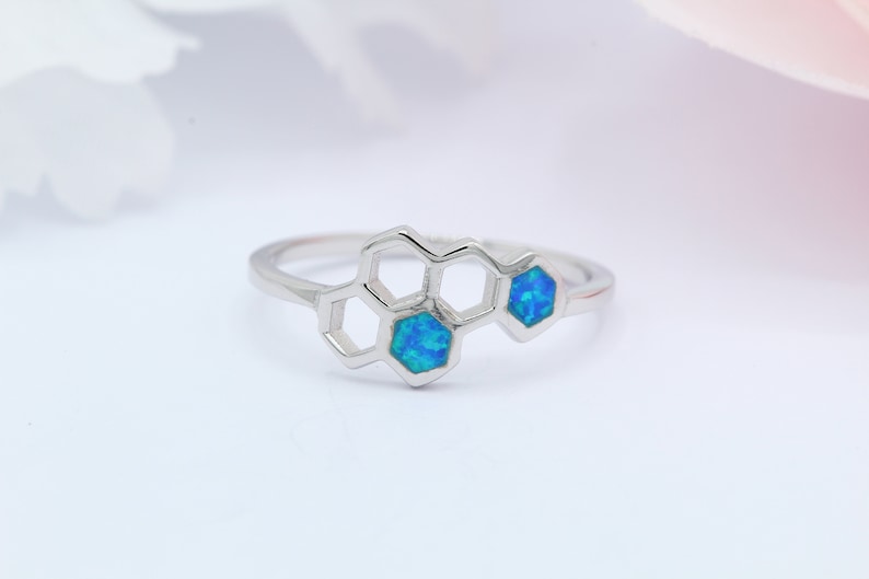 May include: A silver ring featuring a honeycomb design with two blue opal stones.