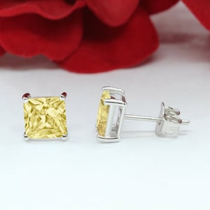 May include: A pair of silver stud earrings with square-shaped yellow gemstones.