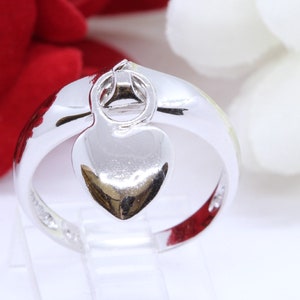 May include: A silver ring with a heart-shaped pendant. The ring is smooth and shiny.