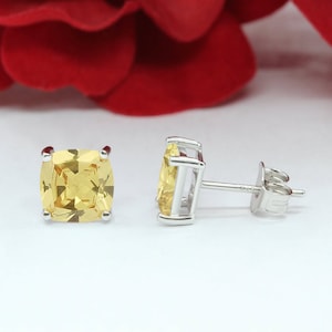 May include: A pair of silver stud earrings with a square-shaped yellow gemstone in each earring.