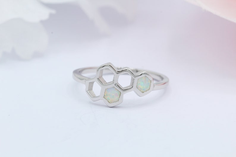 May include: A silver ring with a honeycomb design featuring three white opals.