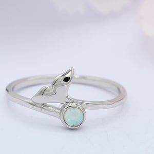 May include: A silver ring featuring a mermaid tail design and a white opal gemstone.