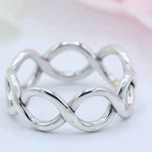 May include: A silver ring with a braided design. The ring is made of a single piece of metal that is twisted and looped to create a unique and intricate pattern.