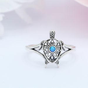 May include: A silver ring featuring a detailed turtle design with a blue opal gemstone in the center.