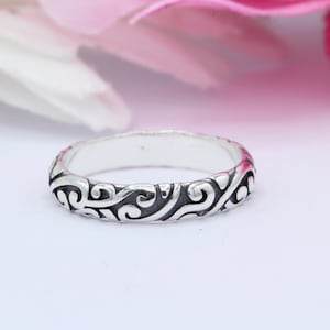May include: A silver ring with a delicate, intricate design of swirling patterns. The ring is thin and has a polished finish.