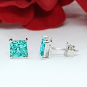 May include: A pair of silver stud earrings with square-shaped turquoise gemstones.