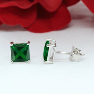 May include: A pair of silver stud earrings with square emerald green gemstones.