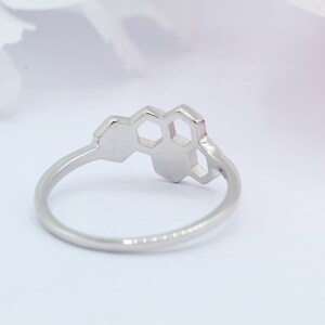 May include: A silver ring featuring a honeycomb design. The ring is made of metal and has a smooth finish.