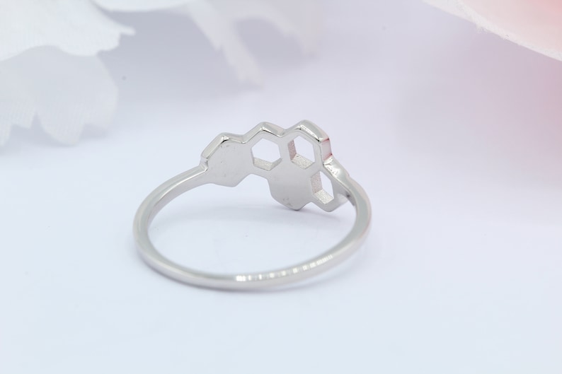 May include: A silver ring featuring a honeycomb design. The ring is made of metal and has a smooth finish.